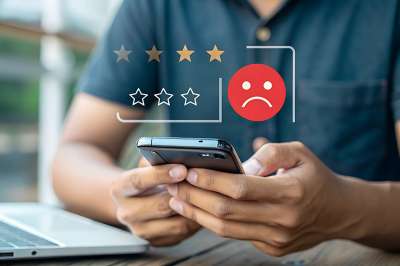 Mann bedient Smartphone, darüber negatives Smiley und schlechte Sterne Bewertung